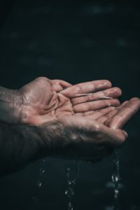 Clear water drips from a pair of cupped hands.