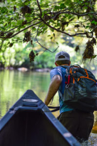 Phillip Bumpers pulls a canoe through woods toward water.