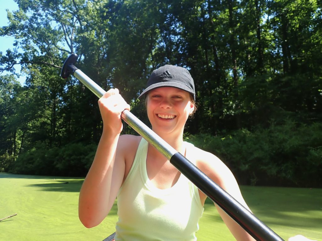 Ally Whiteis, Odum undergraduate, paddles a canoe on a wolffia-covered pond.