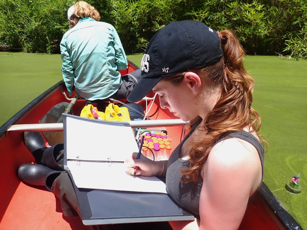 Olivia Allen, Odum undergraduate, sitting behind Laura Naslund in a field canoe and recording data.