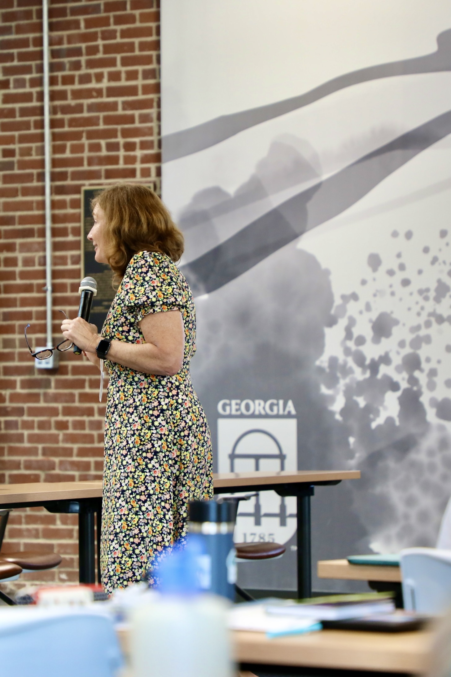 A woman in a floral dress speaks to a crowd.