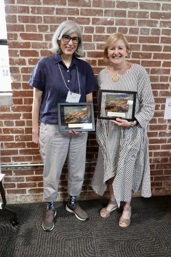 Two women pose, holding awards. 