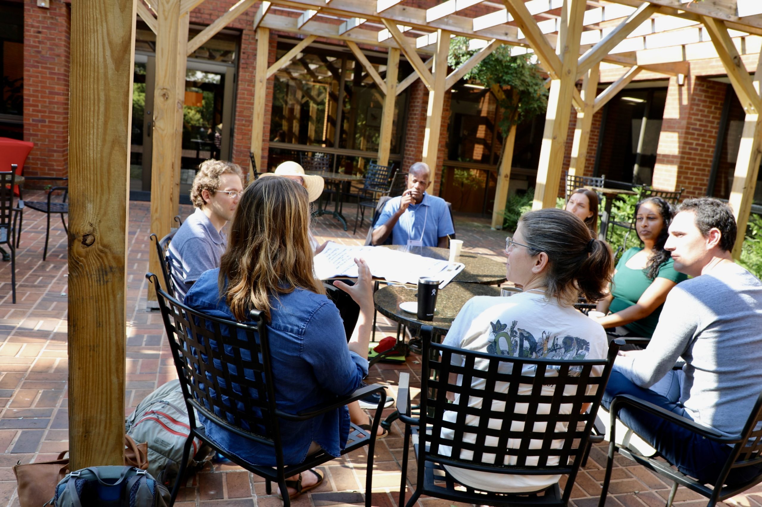 A group discusses something outside in a sunny courtyard.