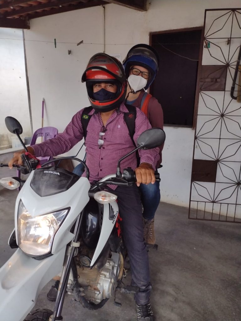 Two people with helmets sitting on a white motorcycle on the porch of a house.