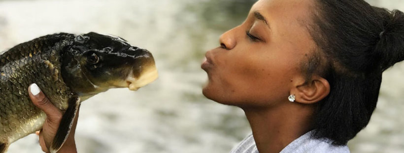 A woman holds a fish, pretending to kiss it.