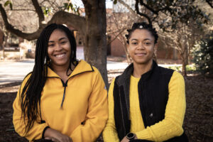 Two women stand in front of the Odum School of Ecology building.