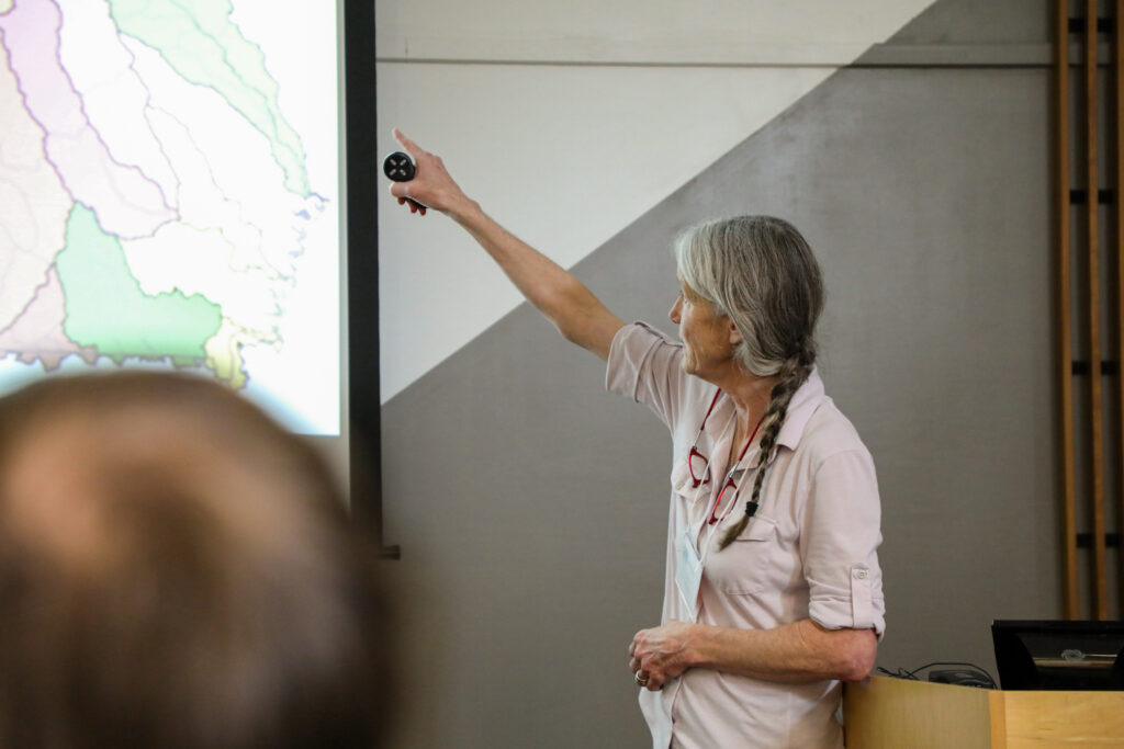 A silver-haired woman points to a feature on a projector screen.