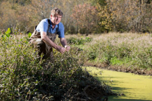 Prof. Darold Batzer kneels next to green water.