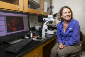 Prof. Susan Wilde sits at a lab bench with a microscope behind her.