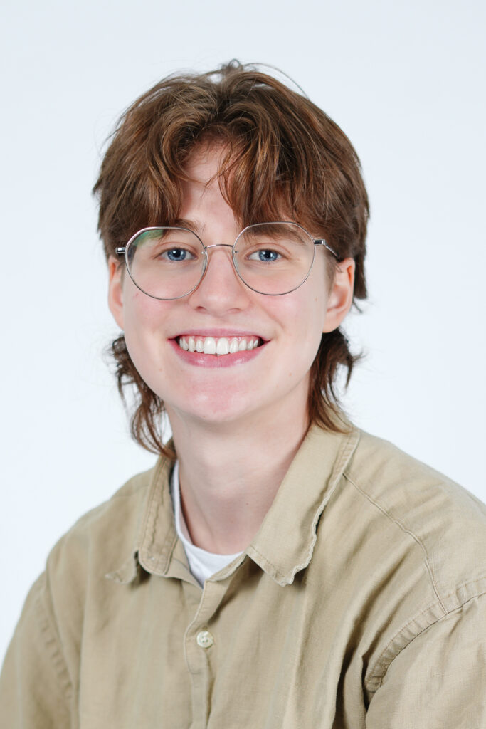 A short-haired person smiles in glasses and a button-down.