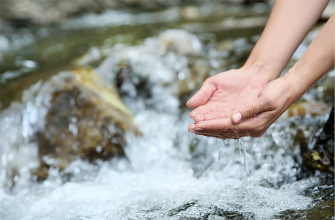 Cupped hands held above a rushing stream.